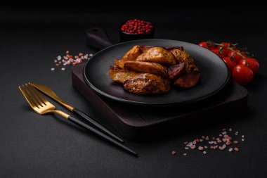 Lezzetli ızgara patates dilimleri, sarımsak, baharat ve otlar koyu beton arka planda.