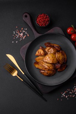 Lezzetli ızgara patates dilimleri, sarımsak, baharat ve otlar koyu beton arka planda.