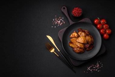 Lezzetli ızgara patates dilimleri, sarımsak, baharat ve otlar koyu beton arka planda.