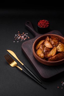 Lezzetli ızgara patates dilimleri, sarımsak, baharat ve otlar koyu beton arka planda.