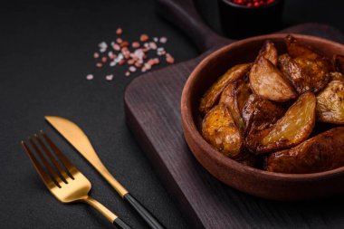 Lezzetli ızgara patates dilimleri, sarımsak, baharat ve otlar koyu beton arka planda.