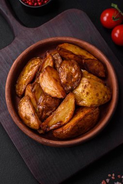 Lezzetli ızgara patates dilimleri, sarımsak, baharat ve otlar koyu beton arka planda.