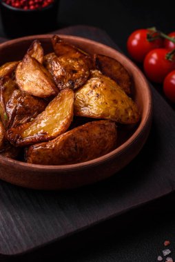 Lezzetli ızgara patates dilimleri, sarımsak, baharat ve otlar koyu beton arka planda.