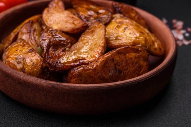 Lezzetli ızgara patates dilimleri, sarımsak, baharat ve otlar koyu beton arka planda.