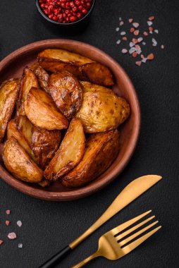 Lezzetli ızgara patates dilimleri, sarımsak, baharat ve otlar koyu beton arka planda.