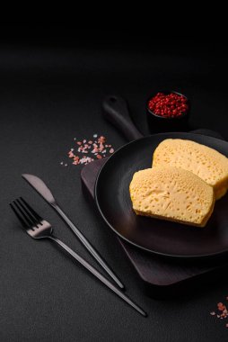 Sütlü, baharatlı ve otlu leziz omlet koyu beton arka planda seramik bir tabakta büyük parçalar halinde kesilmiş.