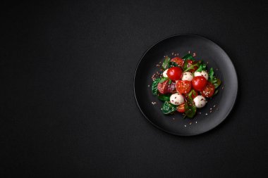 Mozarella peynirli lezzetli taze salata, kiraz domatesleri, otlar, tuz ve baharatlar koyu beton arka planda.