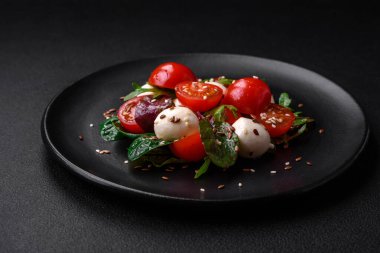 Mozarella peynirli lezzetli taze salata, kiraz domatesleri, otlar, tuz ve baharatlar koyu beton arka planda.
