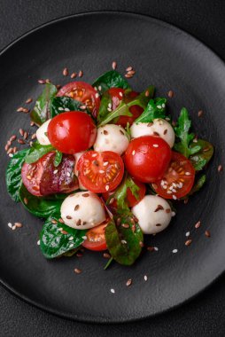 Mozarella peynirli lezzetli taze salata, kiraz domatesleri, otlar, tuz ve baharatlar koyu beton arka planda.