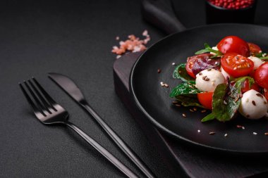 Mozarella peynirli lezzetli taze salata, kiraz domatesleri, otlar, tuz ve baharatlar koyu beton arka planda.