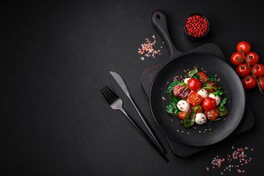 Mozarella peynirli lezzetli taze salata, kiraz domatesleri, otlar, tuz ve baharatlar koyu beton arka planda.