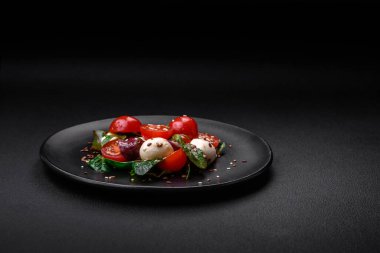 Mozarella peynirli lezzetli taze salata, kiraz domatesleri, otlar, tuz ve baharatlar koyu beton arka planda.