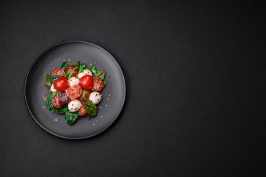 Mozarella peynirli lezzetli taze salata, kiraz domatesleri, otlar, tuz ve baharatlar koyu beton arka planda.
