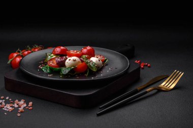 Mozarella peynirli lezzetli taze salata, kiraz domatesleri, otlar, tuz ve baharatlar koyu beton arka planda.