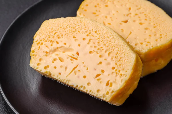 美味的多孔黄色奶酪 在深色混凝土底座上的陶瓷盘上切成大块 — 图库照片