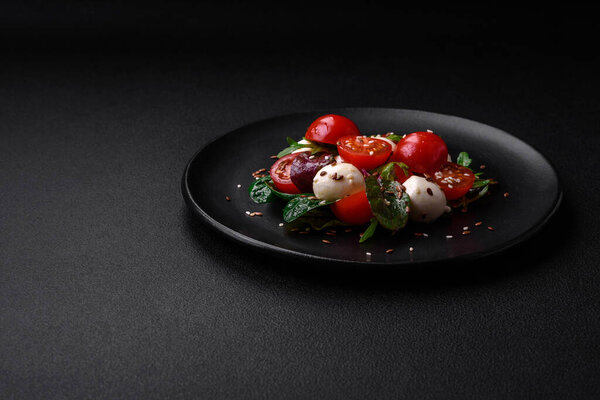 Delicious fresh salad with mozzarella cheese, cherry tomatoes, herbs, salt and spices on a dark concrete background