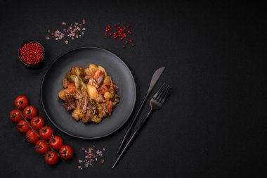 Patatesli, domatesli, biftekli, soğanlı ve havuçlu lezzetli güveç. Koyu beton arka planda seramik bir tabakta.