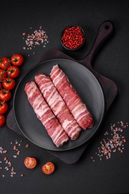 Pastırmaya sarılmış tuzlu ve baharatlı çiğ et veya koyu beton arka planda cevapcici.