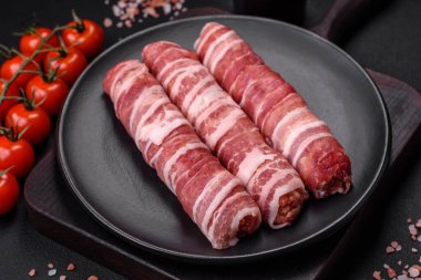 Pastırmaya sarılmış tuzlu ve baharatlı çiğ et veya koyu beton arka planda cevapcici.