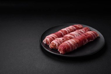 Pastırmaya sarılmış tuzlu ve baharatlı çiğ et veya koyu beton arka planda cevapcici.