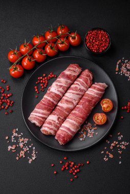 Pastırmaya sarılmış tuzlu ve baharatlı çiğ et veya koyu beton arka planda cevapcici.