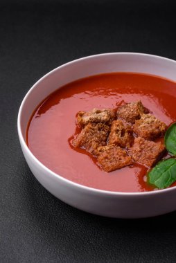 Koyu beton bir zeminde seramik tabakta ekmek kırıntıları, tuz ve baharatlarla nefis taze gazpacho.