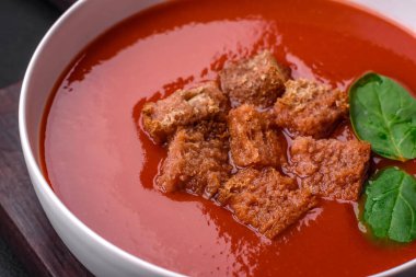 Koyu beton bir zeminde seramik tabakta ekmek kırıntıları, tuz ve baharatlarla nefis taze gazpacho.