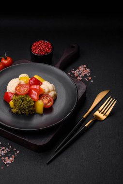 Lezzetli taze brokoli salatası, karnabahar, tatlı biber ve baharatlı kiraz domatesleri ve koyu beton arka planda tuz.