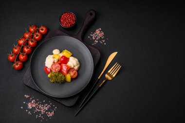 Lezzetli taze brokoli salatası, karnabahar, tatlı biber ve baharatlı kiraz domatesleri ve koyu beton arka planda tuz.