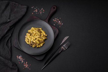 Yeşil pesto soslu lezzetli fusilli makarna, koyu beton bir zeminde seramik tabakta tuz ve baharatlar.