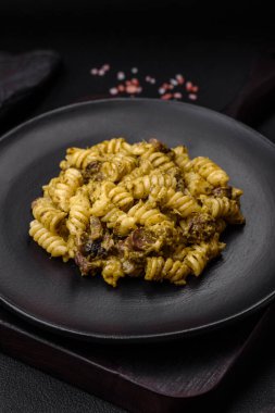 Yeşil pesto soslu lezzetli fusilli makarna, koyu beton bir zeminde seramik tabakta tuz ve baharatlar.