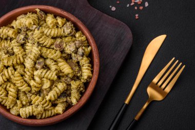 Yeşil pesto soslu lezzetli fusilli makarna, koyu beton bir zeminde seramik tabakta tuz ve baharatlar.