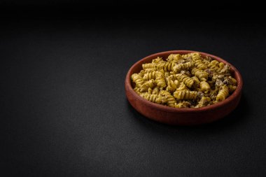 Yeşil pesto soslu lezzetli fusilli makarna, koyu beton bir zeminde seramik tabakta tuz ve baharatlar.
