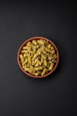 Yeşil pesto soslu lezzetli fusilli makarna, koyu beton bir zeminde seramik tabakta tuz ve baharatlar.
