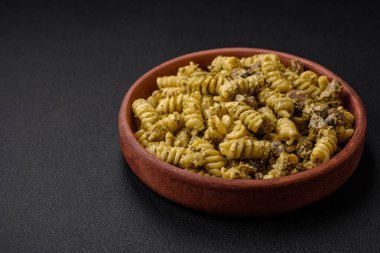 Yeşil pesto soslu lezzetli fusilli makarna, koyu beton bir zeminde seramik tabakta tuz ve baharatlar.