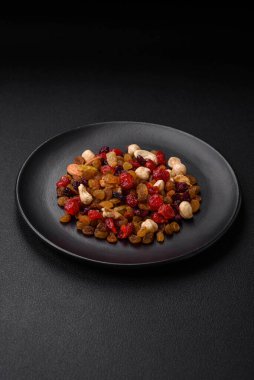 Kavrulmuş kaju, fındık ve ceviz karışımı, koyu beton arka planda kurutulmuş kızılcık ve kuru üzümler.