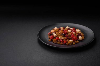 Kavrulmuş kaju, fındık ve ceviz karışımı, koyu beton arka planda kurutulmuş kızılcık ve kuru üzümler.