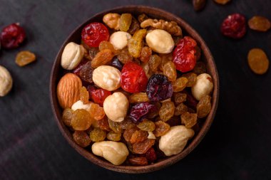 Kavrulmuş kaju, fındık ve ceviz karışımı, koyu beton arka planda kurutulmuş kızılcık ve kuru üzümler.