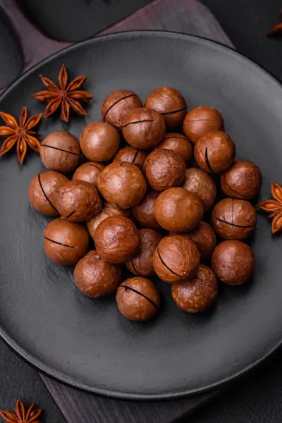 stock image Delicious roasted macadamia nuts in shell on a dark textured concrete background. Vegetarian food