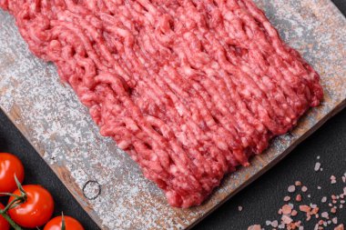 Ahşap kesme tahtasındaki çiğ et ya da domuz eti, baharatlar ve koyu beton arka planda tuz.