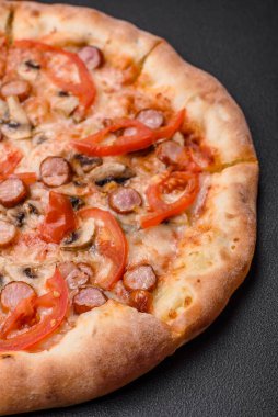 Füme sosisli Bavyera pizzası, domates, peynir, tuz ve baharatlar koyu beton arka planda.