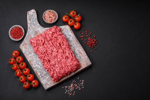 stock image Raw ground beef or pork on a wooden cutting board with spices and salt on a dark concrete background