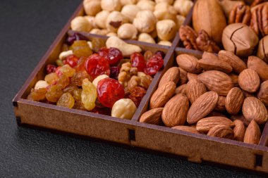 Kavrulmuş macadamia fındığı, ceviz, ceviz, ceviz, badem, kuru üzüm karışımı koyu beton bir arka planda.