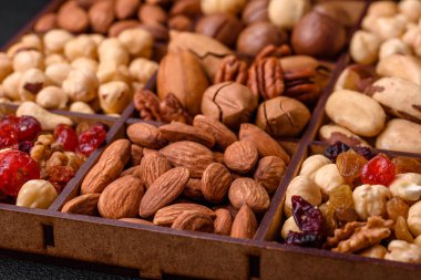 Kavrulmuş macadamia fındığı, ceviz, ceviz, ceviz, badem, kuru üzüm karışımı koyu beton bir arka planda.