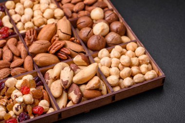 Kavrulmuş macadamia fındığı, ceviz, ceviz, ceviz, badem, kuru üzüm karışımı koyu beton bir arka planda.