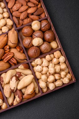 Kavrulmuş macadamia fındığı, ceviz, ceviz, ceviz, badem, kuru üzüm karışımı koyu beton bir arka planda.