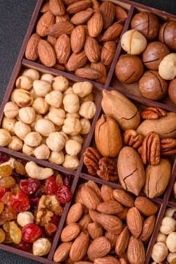 Kavrulmuş macadamia fındığı, ceviz, ceviz, ceviz, badem, kuru üzüm karışımı koyu beton bir arka planda.