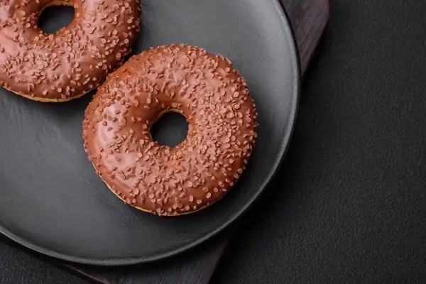 stock image Delicious chocolate glazed donut sprinkled with chocolate chips on a dark concrete background