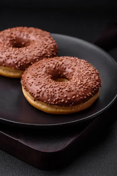 stock image Delicious chocolate glazed donut sprinkled with chocolate chips on a dark concrete background