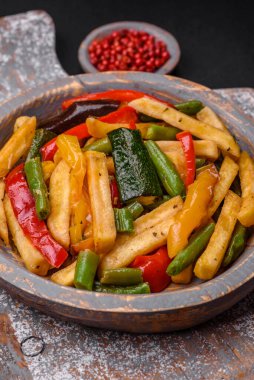 Lezzetli kızarmış patates, dolmalık biber, kuşkonmaz fasulyesi, tuz ve baharatlar, koyu beton bir arka planda.